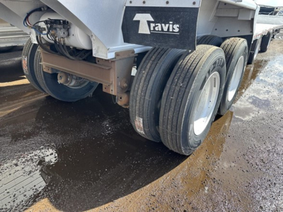 Travis frameless aluminum end dump trailer showing twin rear axles and mudflaps with Travis logo.
