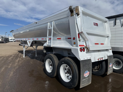 Travis frameless aluminum end dump trailer showing rear and side, dual rear axles, white paint, hydraulic tilt mechanism, reflective tape, and DV decals.