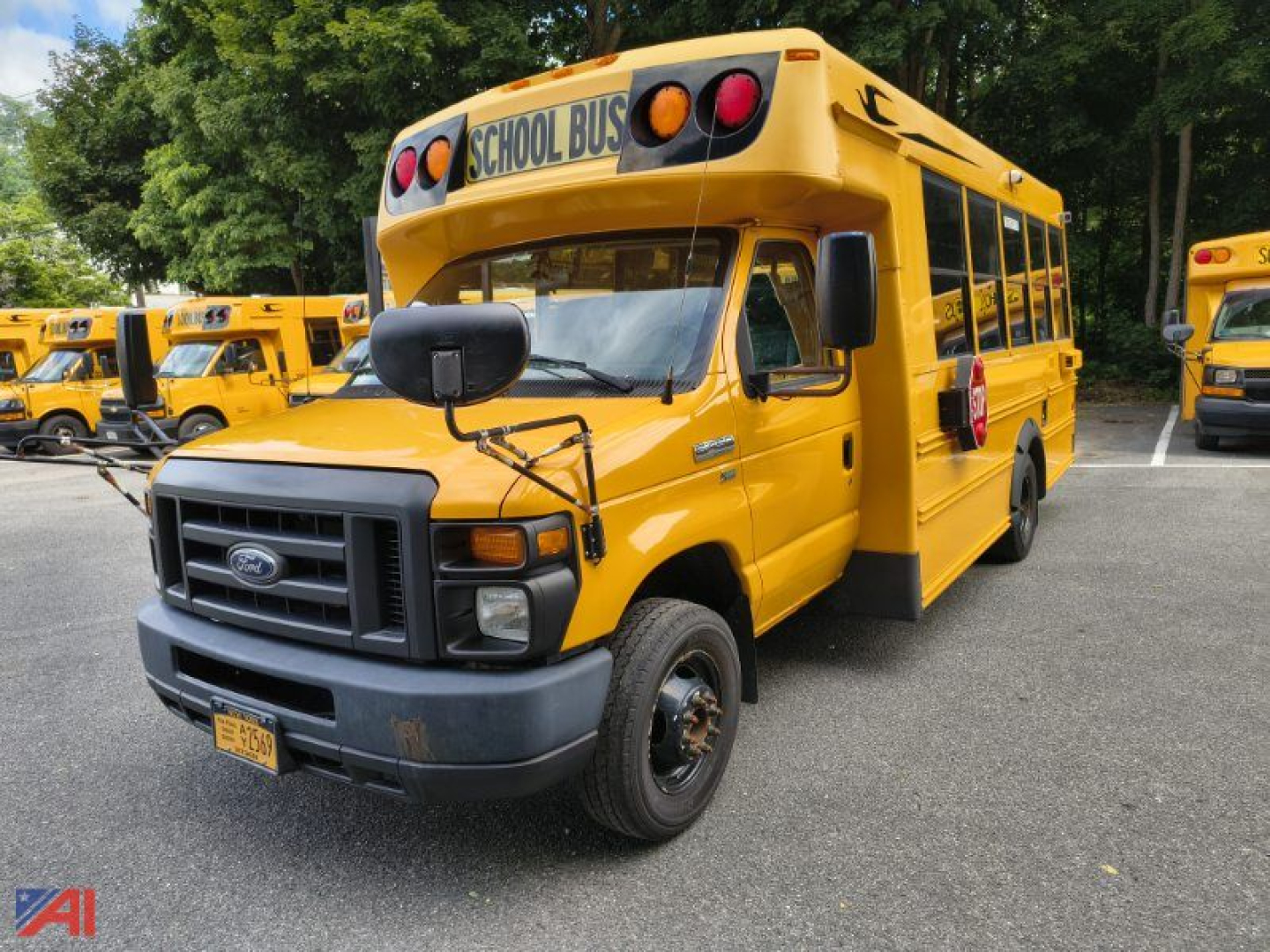 School bus 2016 Ford E-Series front-left view showing yellow bus with black bumper, 'SCHOOL BUS' sign, and side mirrors in a parking lot.
