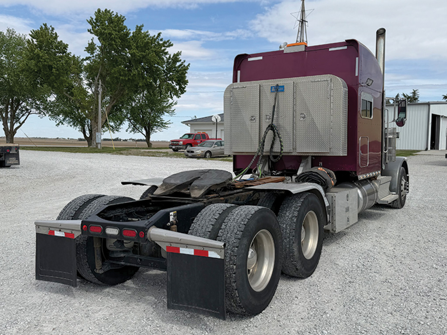 Peterbilt 389 UltraCab rear view showing tractor chassis and dual rear axles under a maroon cab with wind deflector and chrome fuel tanks.