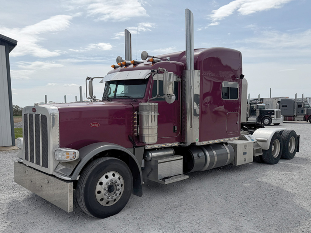 Peterbilt 389 UltraCab conventional sleeper truck in maroon, front three-quarter view, chrome exhaust stacks, dual rear axles, chrome bumper.