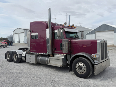 Peterbilt 389 UltraCab tractor in metallic plum color, side view showing long hood, dual exhaust stacks, chrome bumper, and 6x4 rear axles with aluminum fuel tanks.