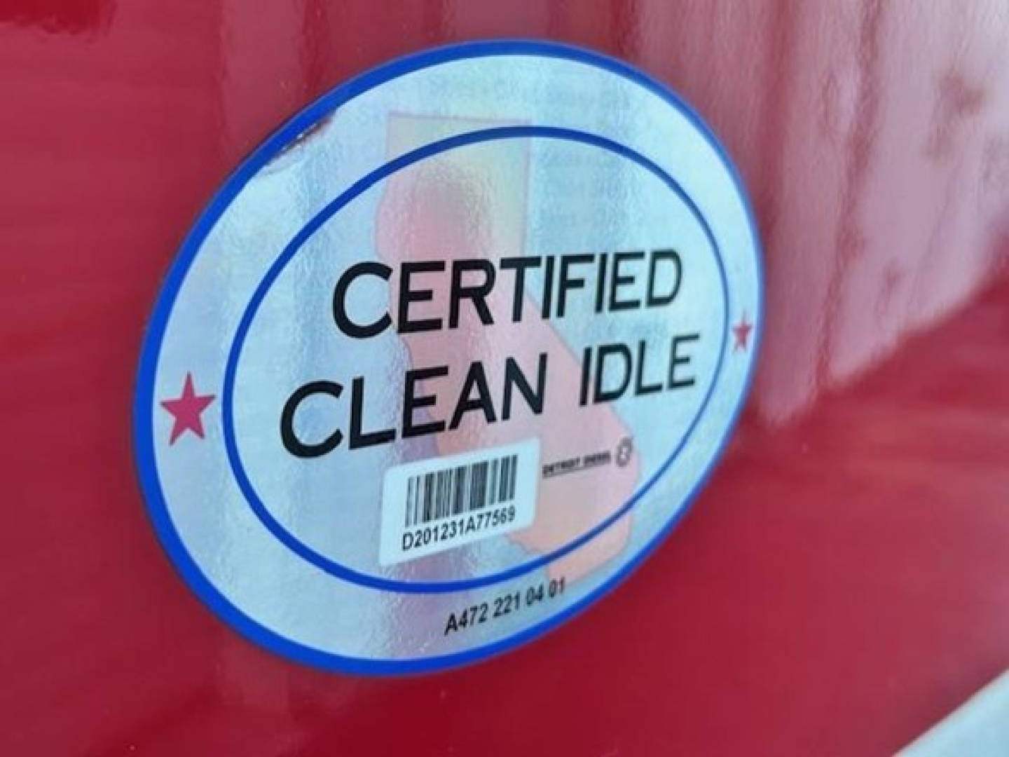 Circular sticker on red vehicle showing 'CERTIFIED CLEAN IDLE' with barcode and small stars.