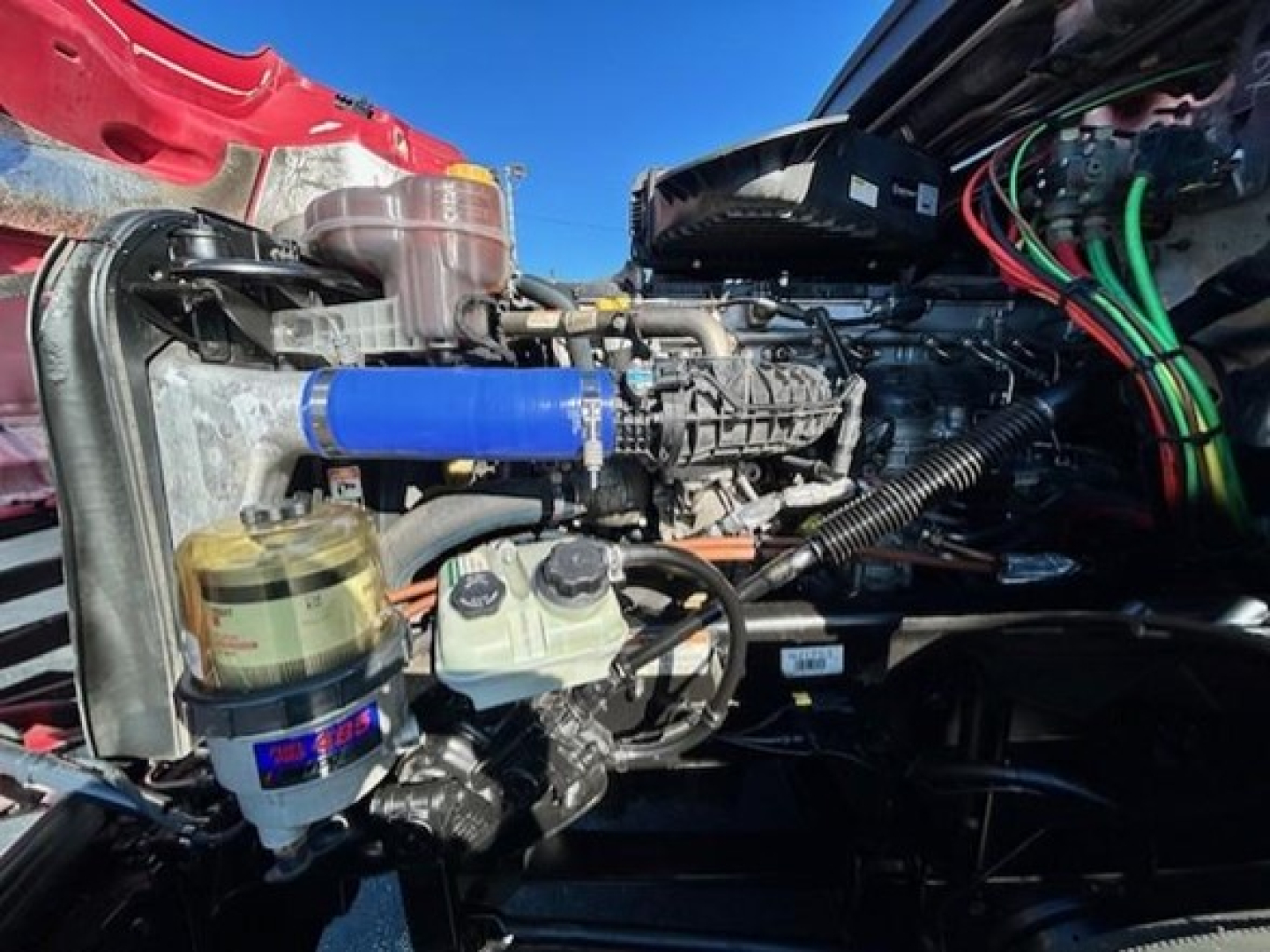 Freightliner Cascadia engine bay showing blue silicone intercooler hose and multiple fluid reservoirs and wiring harnesses.