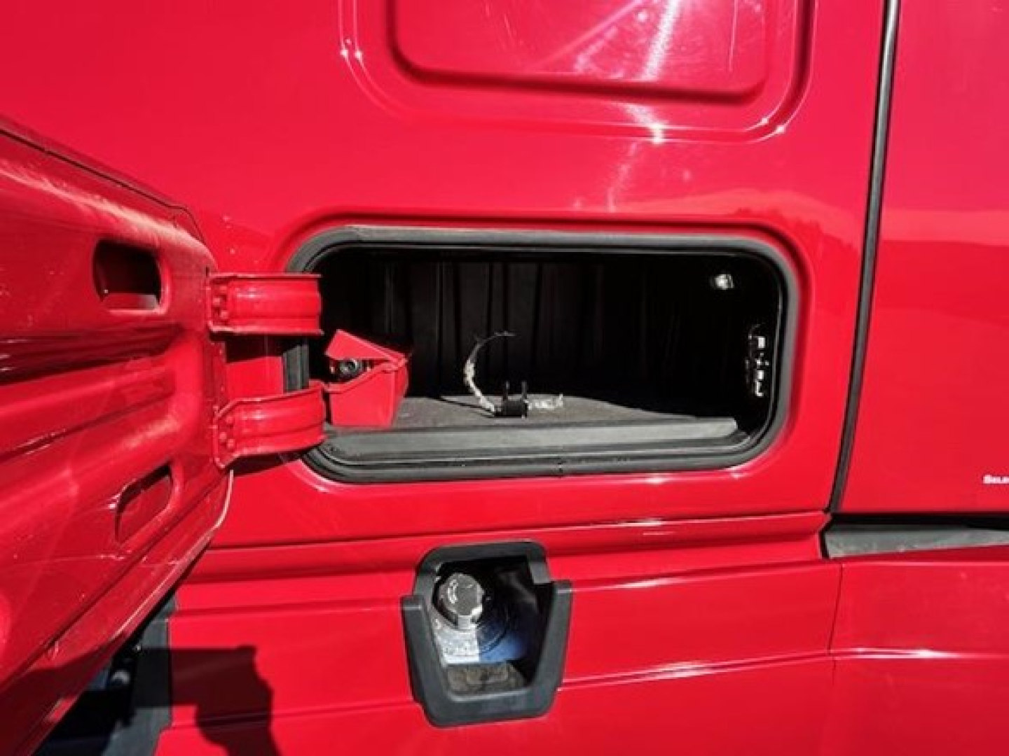 Freightliner Cascadia 126 sleeper cab door open showing side storage compartment and latch in red truck.