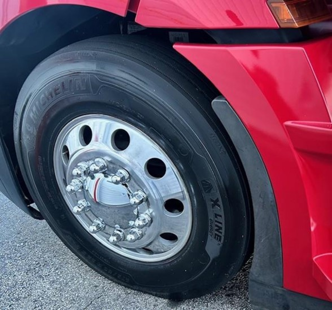 Truck wheel and front fender of a red 2023 Freightliner Cascadia 126 showing Michelin X Line tire and polished aluminum dual rear axle hub.