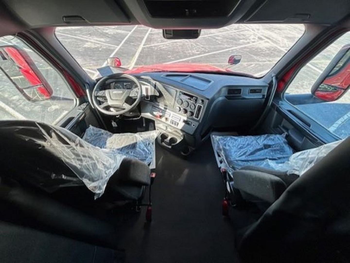 Cab interior of a Freightliner Cascadia truck with steering wheel, dashboard, and seats covered in protective plastic.