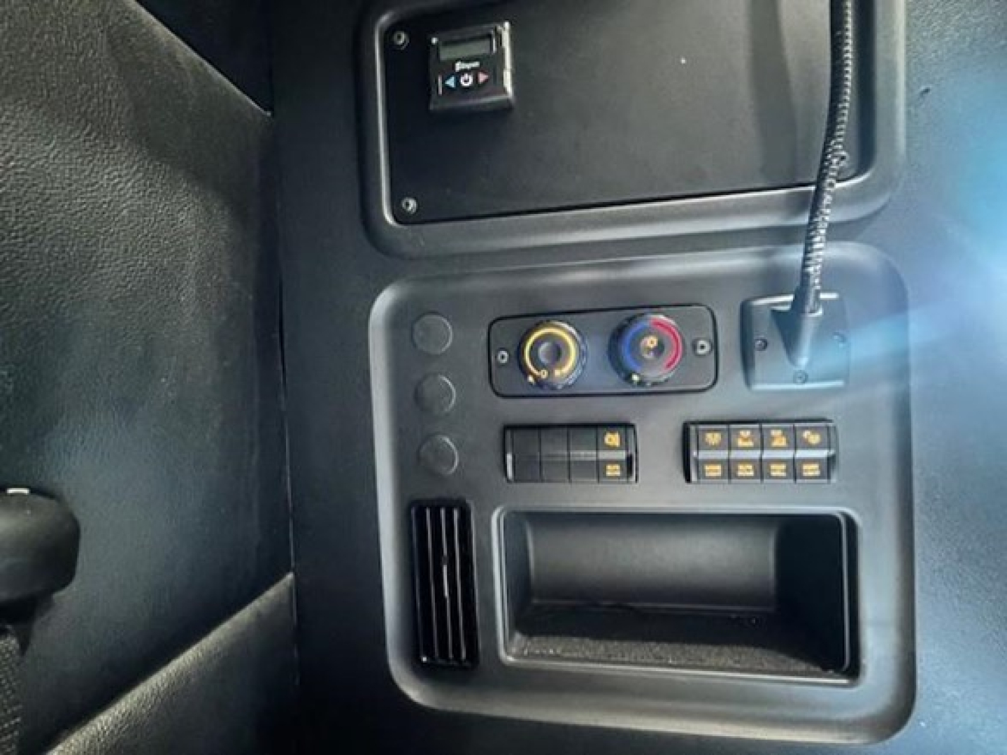 Truck cab interior control panel with two circular knobs and several small switches, USB-like port, and vent/grill area visible.