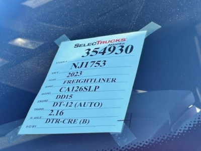 Vehicle tag with listing details: Stock 354930, VIN NJ1753, year 2023, make Freightliner, model CA126SLP, engine DT-12 (AUTO), trans 2.16, rear axle DTR-CRE (B).