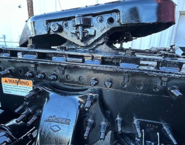 Truck engine bay components showing valve covers and engine block with multiple hoses and bolts; warning sticker visible.