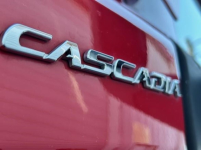 Cascadia emblem on red Freightliner truck side showing metallic 'CASCADIA' badge with reflection.