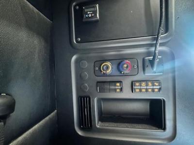 Truck cab interior control panel with two circular knobs and several small switches, USB-like port, and vent/grill area visible.