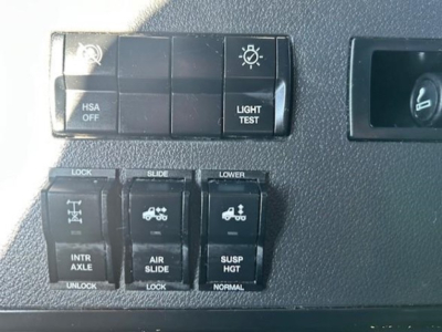 Dashboard switches and controls showing HSA OFF, LIGHT TEST, LOCK, SLIDE, LOWER with icons, INTR AXLE, AIR SLIDE, SUSP HGT, UNLOCK, and corresponding labels.