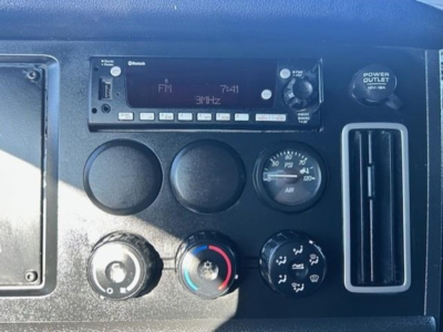 Dashboard of a Freightliner Cascadia showing stereo unit and circular knobs; HVAC controls with blue and red ring, air gauge, and a vertical vent.