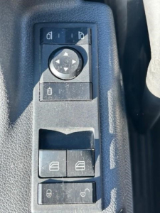Truck door panel controls and window switches in a Freightliner Cascadia cab showing mirror adjust dial and window lock buttons.