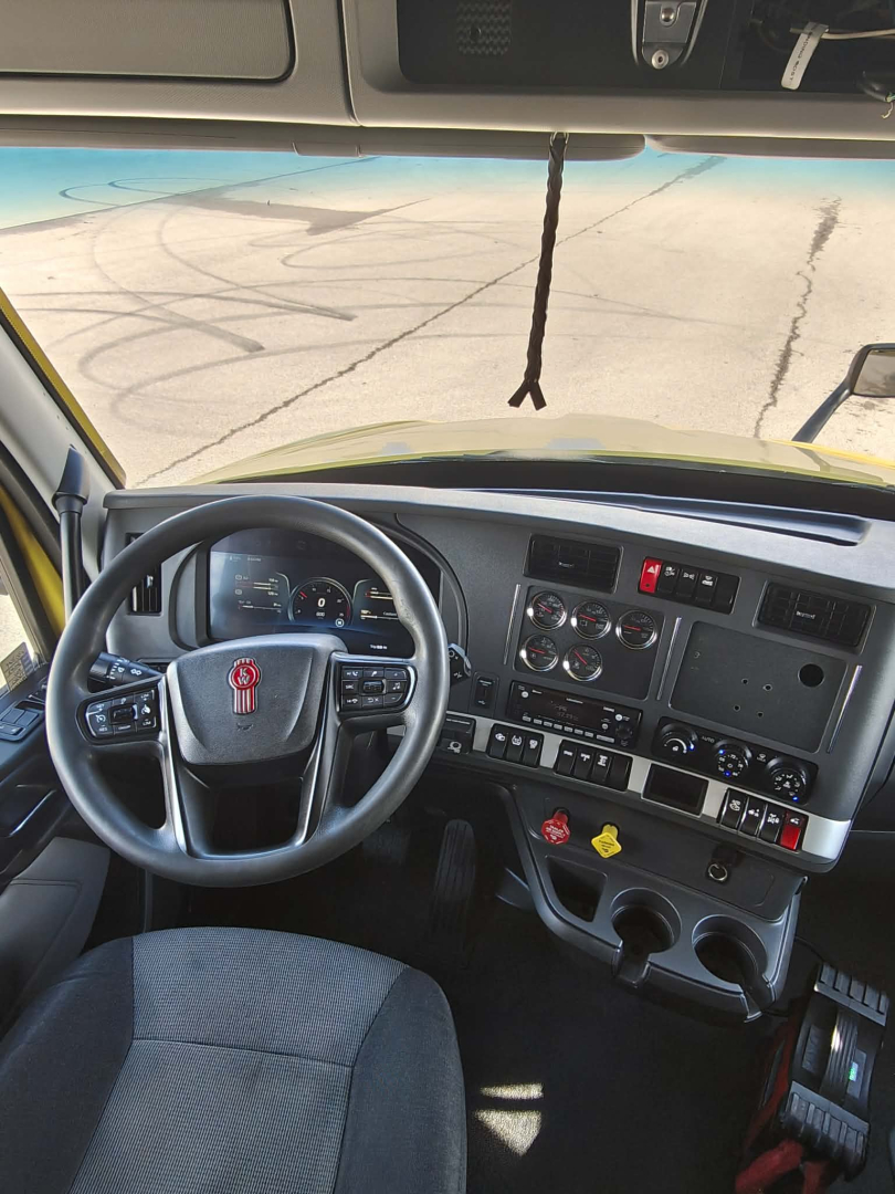 Kenworth T680 cab interior showing steering wheel, instrument cluster, center console, and multiple control switches.