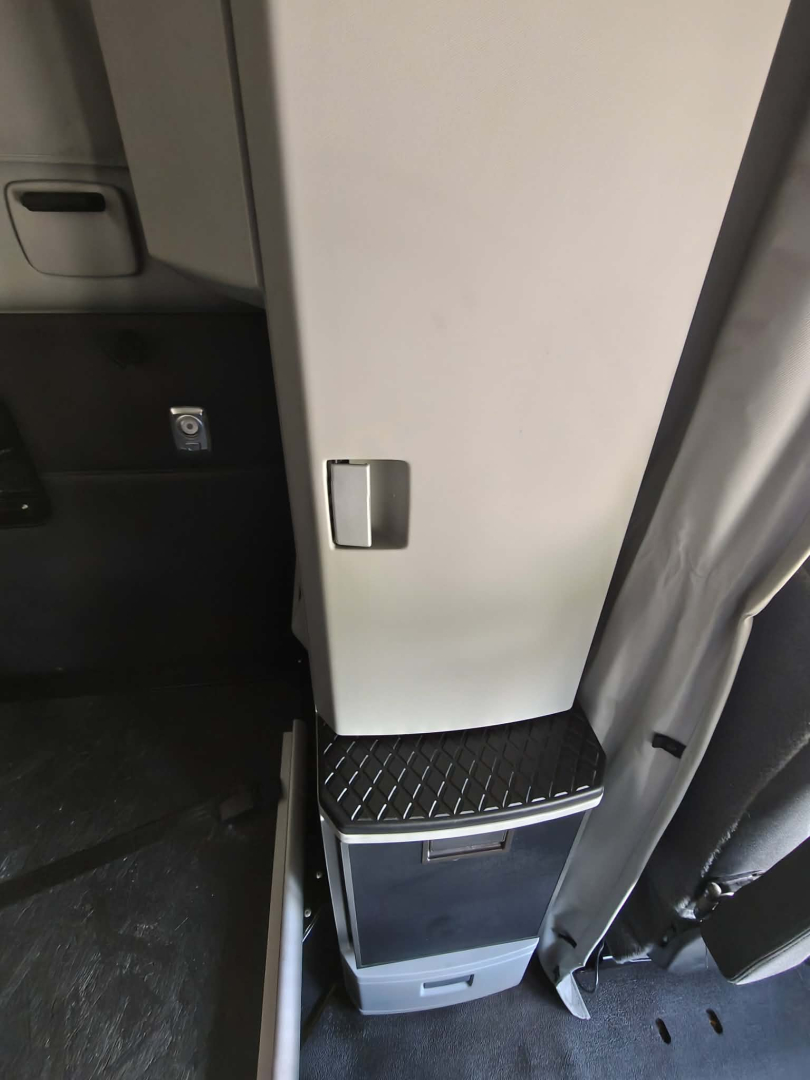 Cab area of a Kenworth T680 interior showing a gray vertical cabinet with a small latch and a diamond-plate step; a small drawer/compartment at base.