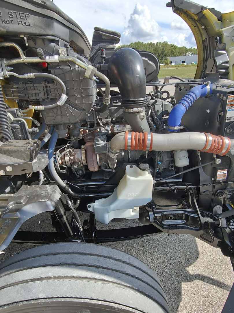 Kenworth T680 engine bay showing coolant reservoir, intercooler pipes, hoses, and turbocharger components in a daytime service area.