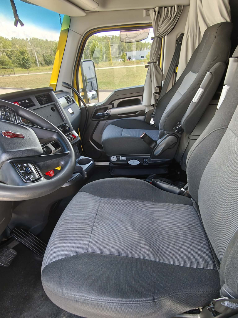 Kenworth T680 truck interior showing driver's seat and passenger seat with steering wheel and dashboard visible.