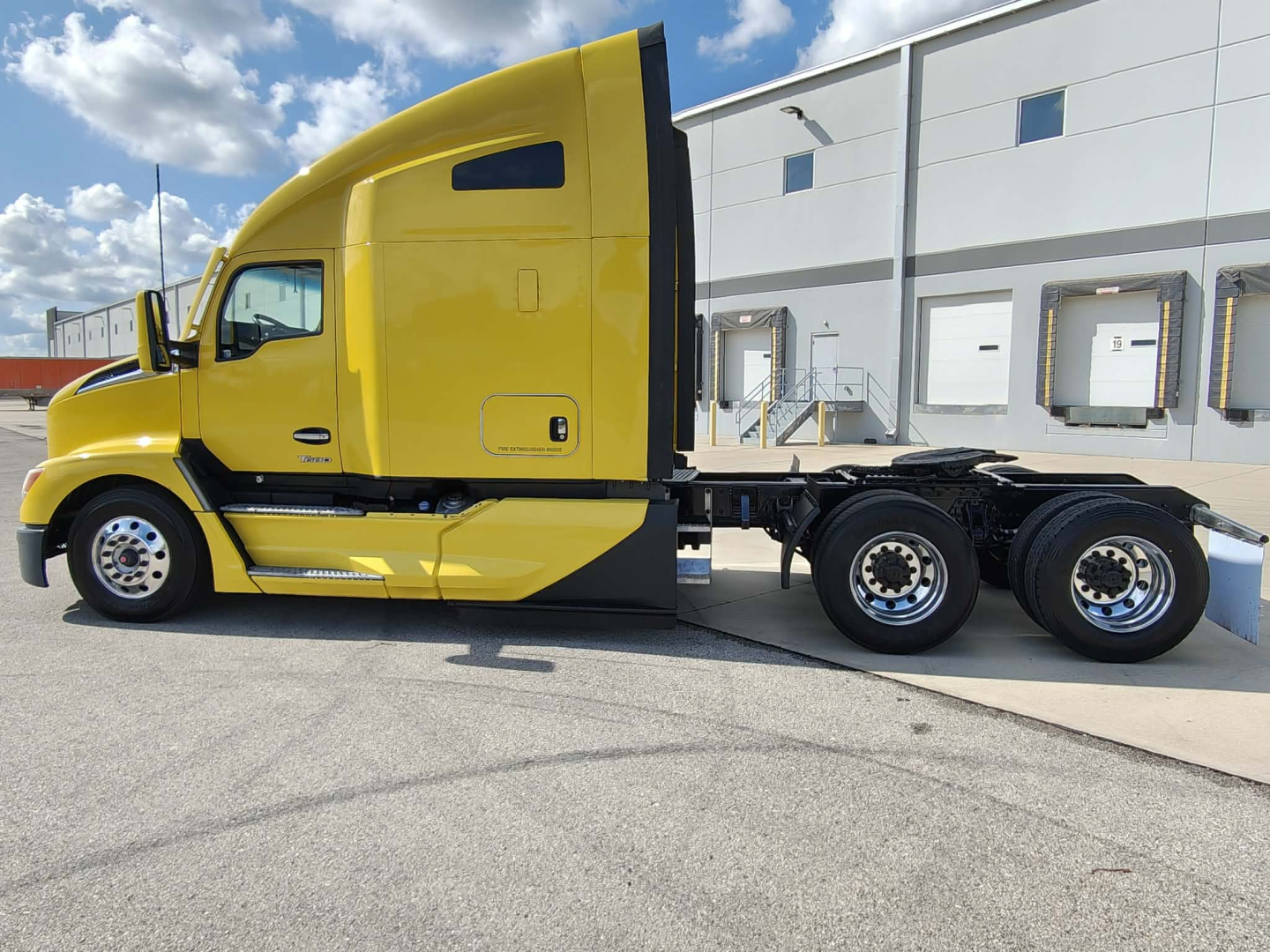 Side view of a bright yellow Kenworth T680 truck chassis with sleeper cab, showing text on the cab and body panels.