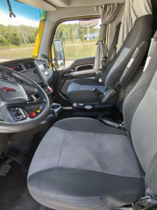 Cab interior of a 2023 Kenworth T680 truck showing driver and passenger seats, steering wheel, dashboard, and window with curtains.