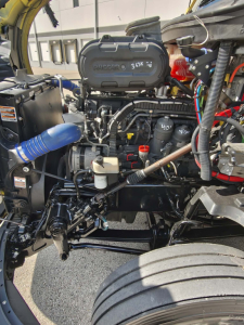 Kenworth T680 engine bay showing air intake, turbo, and various fluid reservoirs with visible labels and hoses.