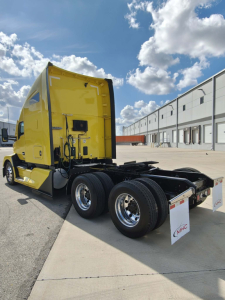 Kenworth T680 tractor in yellow cab, rear view showing dual rear axles and fifth wheel, outdoor lot.