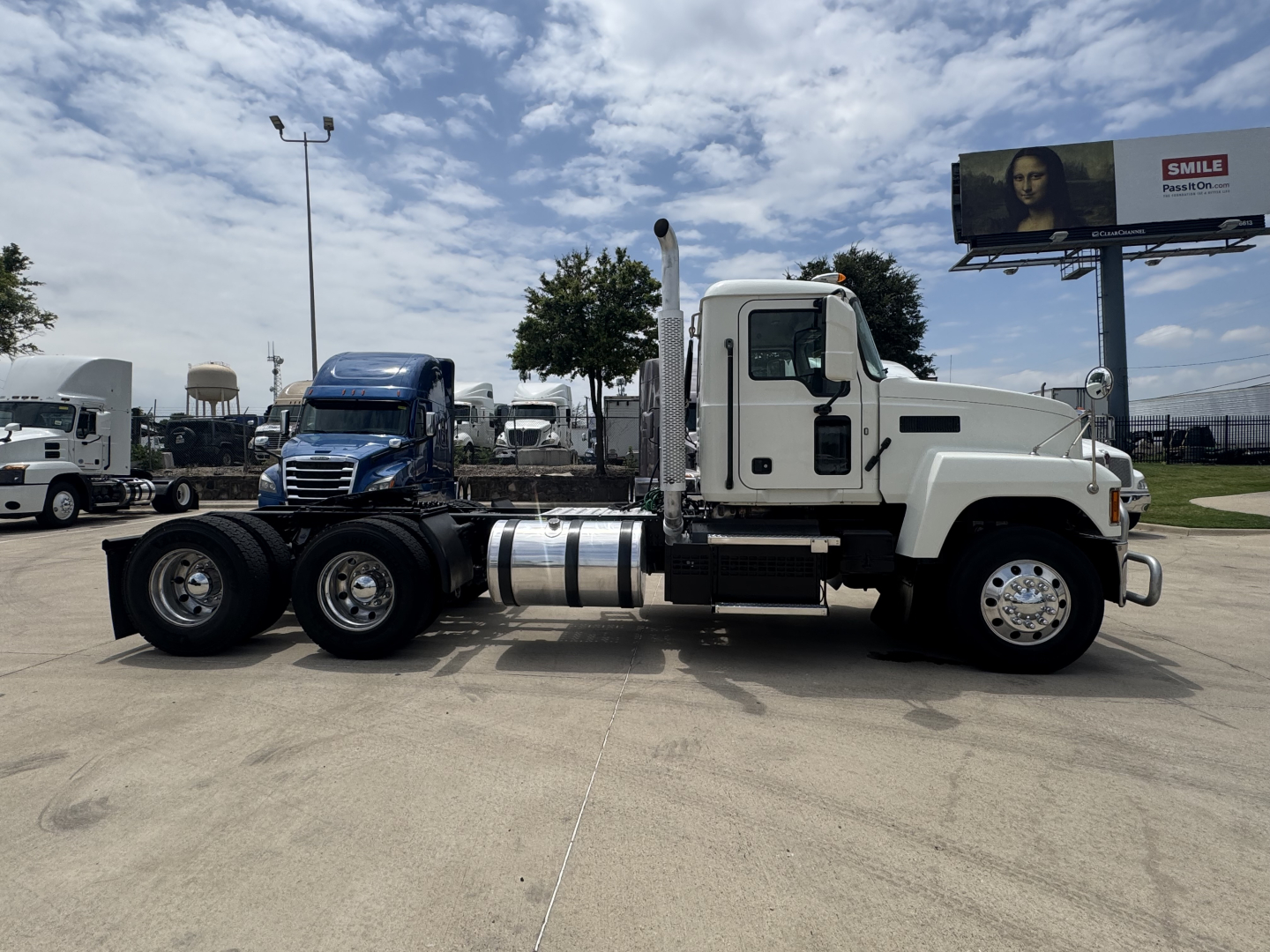 Truck side view of a 2020 Mack PI64T conventional daycab showing white cab, dual rear axles, chrome fuel tanks, and black exhaust stack.