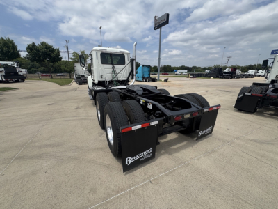 Truck chassis with dual rear axles and fifth wheel seen from rear-left in a dealership lot