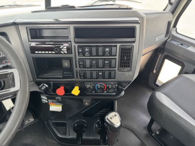 Dashboard of a 2020 Mack PI64T daycab showing steering column, radio, climate controls, and gear shift. Visible instrument panel, switches, and cup holders.