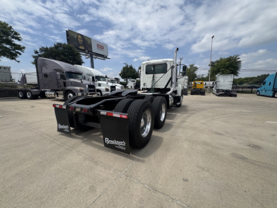 Truck chassis and cab of a 2020 Mack PI64T conventional daycab, rear view showing dual rear axles and mudflaps with Mack logo, in a dealership lot.