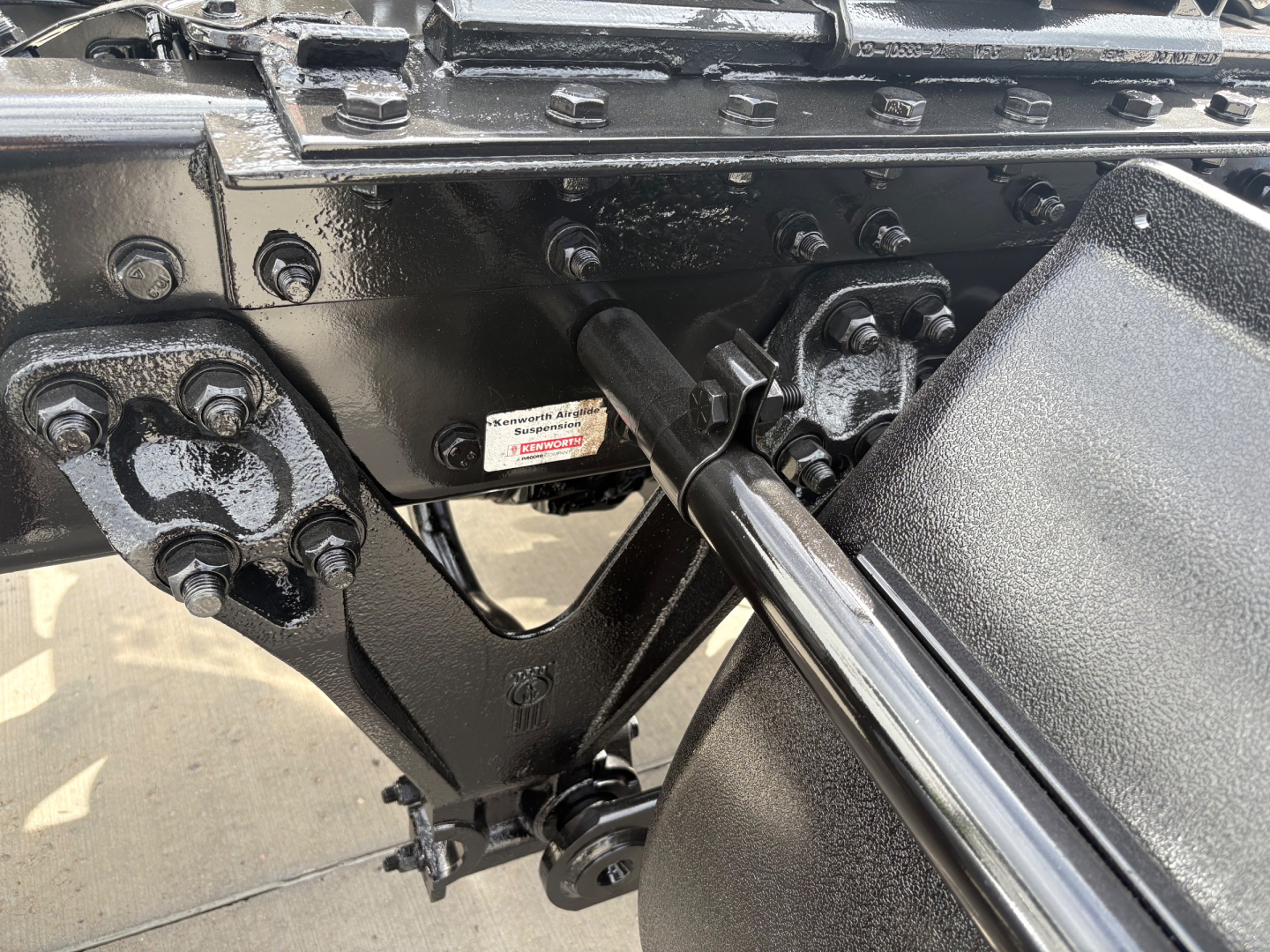 Kenworth T880 chassis showing engine bay area with bolts, linkages, and a label plate.