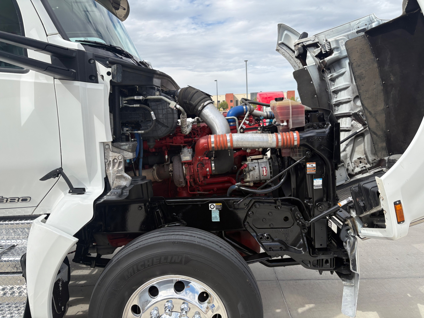 Kenworth T880 engine bay visible with red engine, orange coolant hoses, and exposed components; front left cab open showing mechanicals.