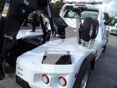 Chevrolet Silverado 6500HD tow truck/tower bed with winch equipment showing white cab and hydraulic arm, spare wheel mounted on rear, control panel on top surface.