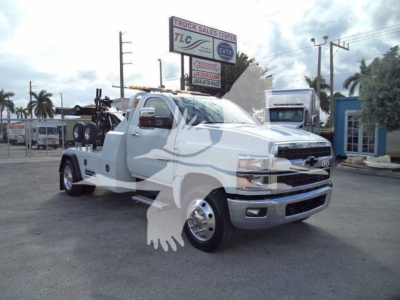 2023 Chevrolet Silverado 6500HD truck in lot showing flatbed with winch setup and spare tires; front grille and headlights visible.