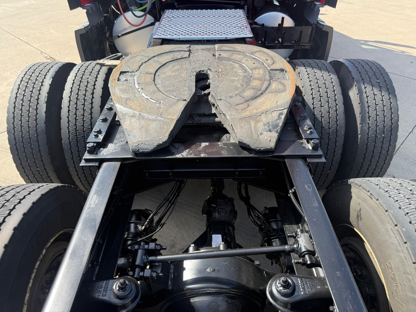 Kenworth T680 chassis and fifth wheel area showing twin rear axles and drivetrain components beneath, with visible suspension components and mountings.