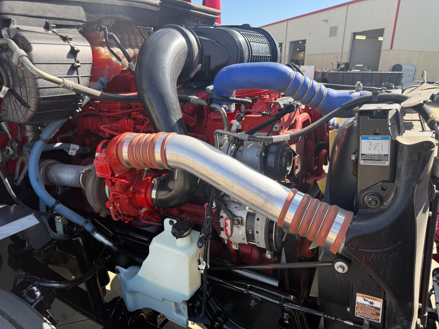 Kenworth T680 engine bay showing turbo hoses, red engine block, blue coolant hose, air intake, and radiator components.