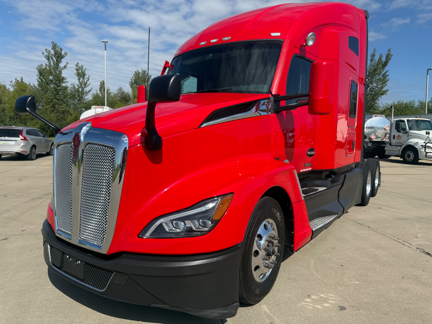 Conventional sleeper truck showing bright red 2023 Kenworth T680 with chrome grille, black lower bumper, and side mirrors. VIN tag not visible; exterior view from front-left.
