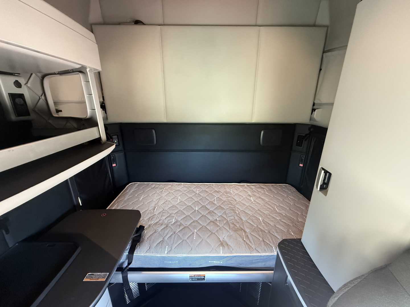 Kenworth T680 sleeper cab interior. View of the bed with a mattress, side storage, and bunk area visible.