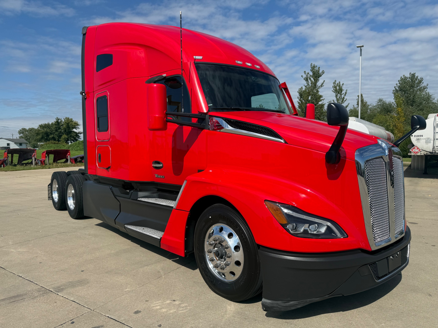 Front-left angle view of a red Kenworth T680 semi-truck with sleeper cab. Visible text includes nothing legible on the truck itself.