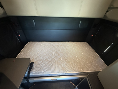 Kenworth T680 truck interior rear sleeper with unfolded bed mattress showing storage compartments.