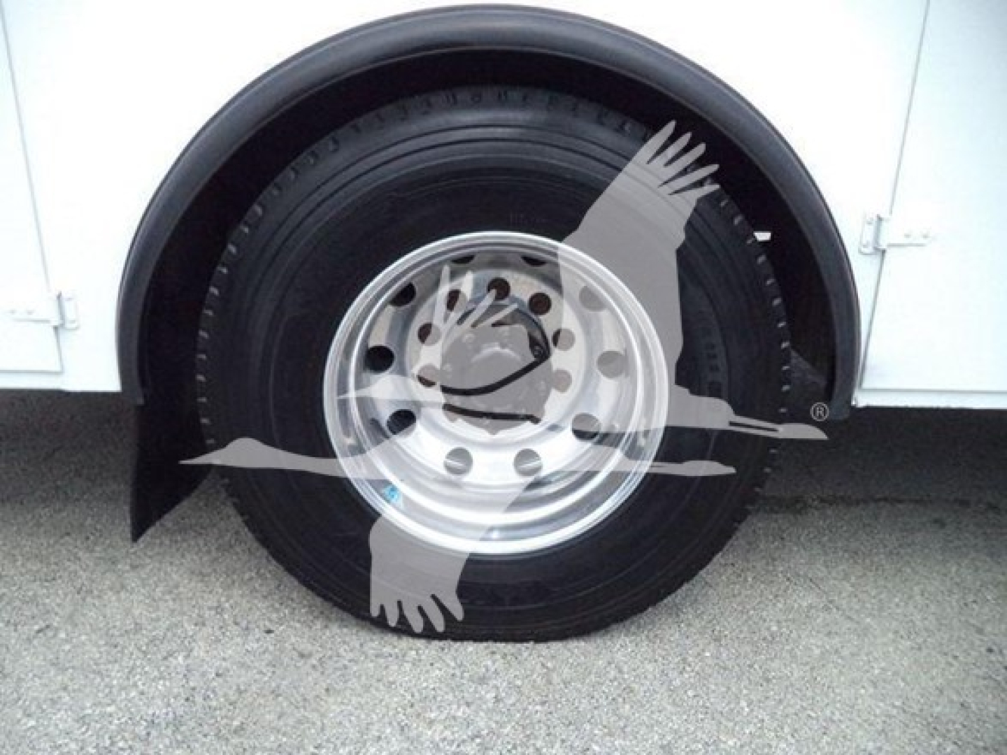 Vehicle wheel close-up on a Kenworth truck fender showing a steel rim and tire with a partial wheel well; watermark of an eagle graphic overlaying the image.