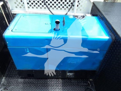 Blue fuel or water tank inside truck bed showing a white bird logo with a cross-like shape, cap and vents on top.