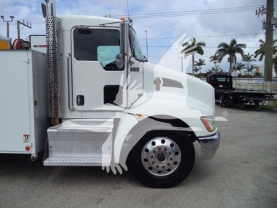 Kenworth T270 truck side view showing cab and front wheel, with a service box adjacent; operational dealership lot background.