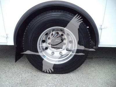 Vehicle wheel close-up on a Kenworth truck fender showing a steel rim and tire with a partial wheel well; watermark of an eagle graphic overlaying the image.