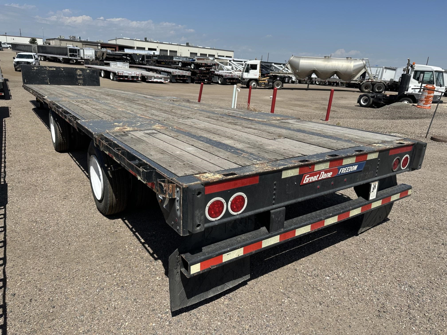 Great Dane spread air steel drop deck trailer with wood deck, rear view showing dual axles, taillights, and reflective tape.