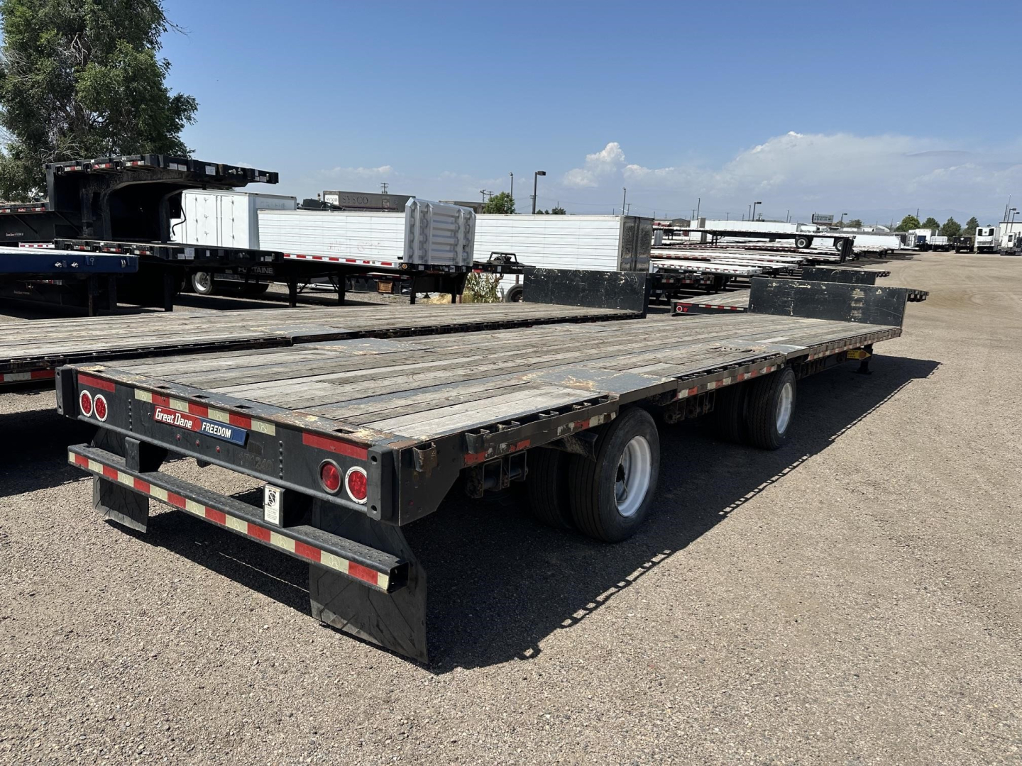 Great Dane spread air steel drop deck trailer with wood decking and triple axles, viewed from rear-right side in a storage lot.
