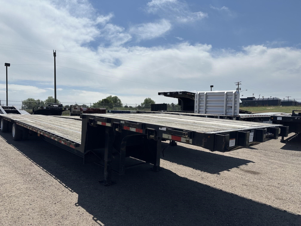 Great Dane spread air steel drop deck trailer with wood deck in a used condition, low-profile landing gear visible, open cargo area, gray sky.