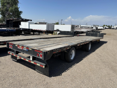 Great Dane spread air steel drop deck trailer with wood decking and triple axles, viewed from rear-right side in a storage lot.