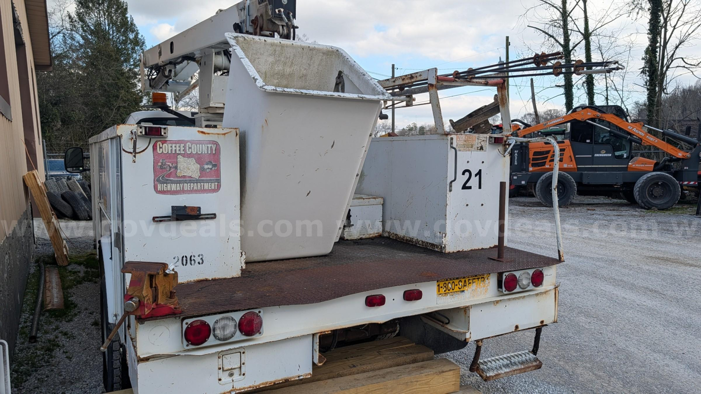 Truck bed of a used 2000 Ford F-550 bucket truck showing a white utility platform with hydraulic boom components in a yard.